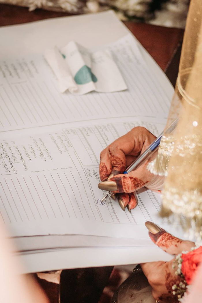 Close-up of henna-decorated hand writing on document, symbolizing culture.